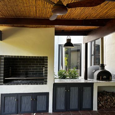 Outdoor kitchen with built-in grill and wood-fired oven under bamboo ceiling.