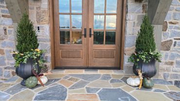 Symmetrical autumnal entrance with potted evergreens and decorative pumpkins.