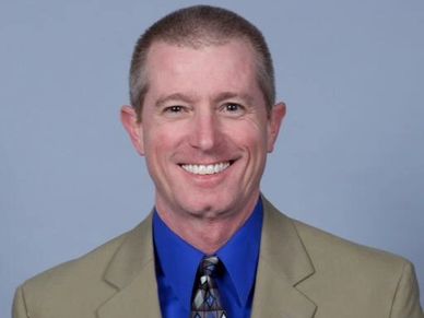Smiling man in beige suit jacket and blue shirt.