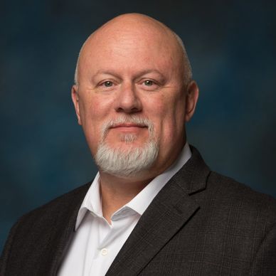 Smiling bald man with white beard in suit.