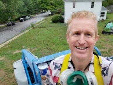 Man smiling on a blue lift with a respirator mask around his neck.