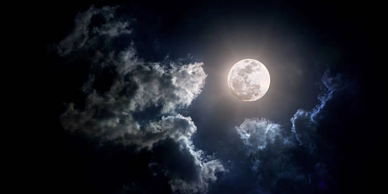 Full moon in sky surrounded by clouds.