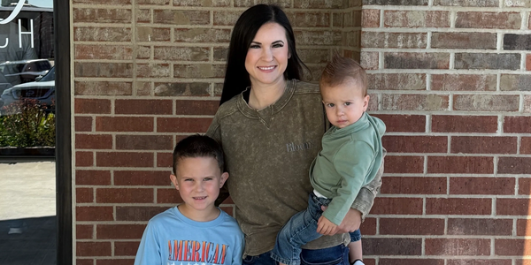 A woman smiling with two young boys in front of a brick wall.