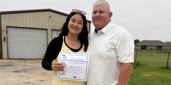 Young woman proudly holding two certificates standing next to an older man outdoors.