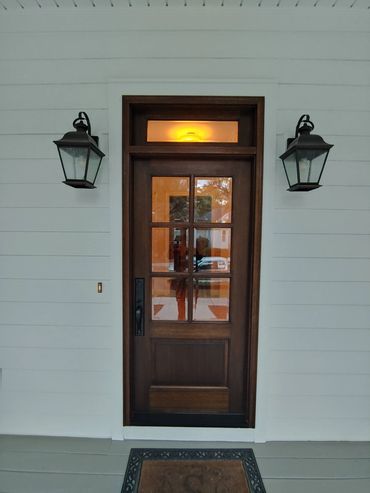 Wooden front door with glass panels and two wall lanterns.