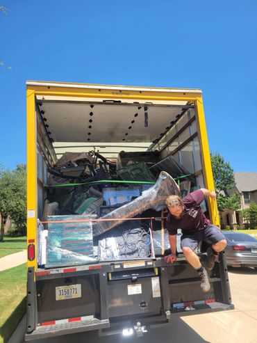Man climbing off a moving truck loaded with furniture.