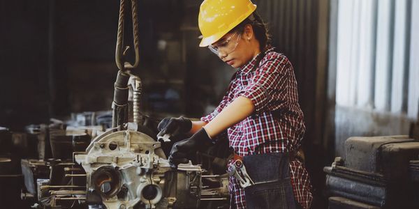 Woman engineer working on machinery wearing safety gear in an industrial setting.