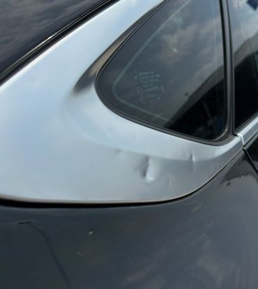 Dents on a silver car panel near the rear window.