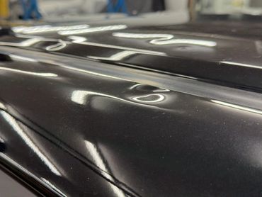 Close-up of a dent on a shiny black surface with reflections of lights.