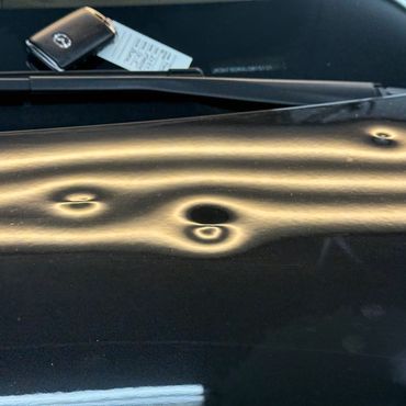 Close-up of car surface with multiple dents and a key fob on the windshield.