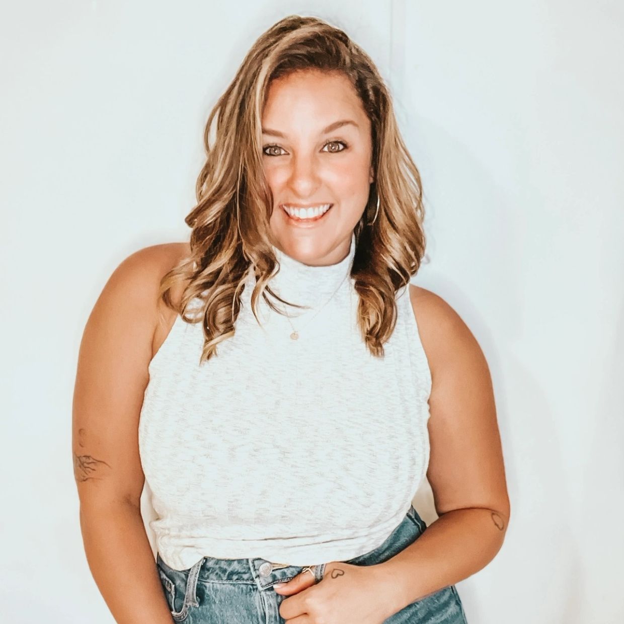 Smiling woman with curly hair in white top and jeans.
