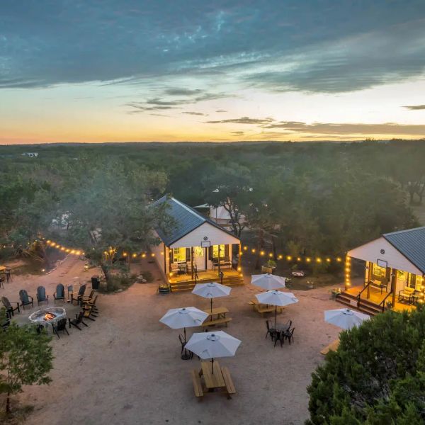 Cozy outdoor cabins with string lights and picnic tables at sunset.