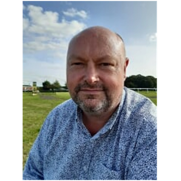 Man with a beard smiling outdoors.