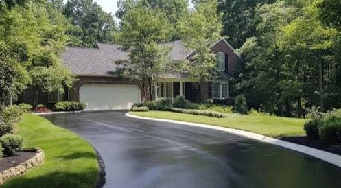 A freshly paved driveway leading to a suburban house surrounded by greenery.