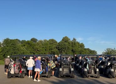 Golfers preparing with carts on a sunny day near trees.