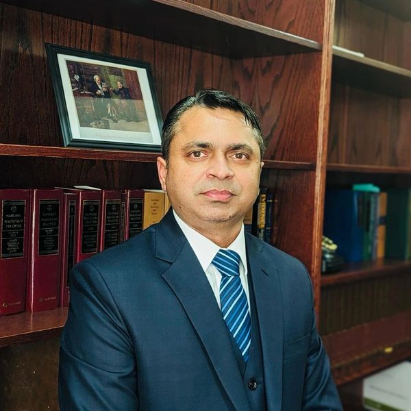 Man in suit posing in front of a bookshelf.