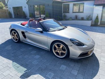 Silver Porsche convertible parked on a driveway with bronze wheels.