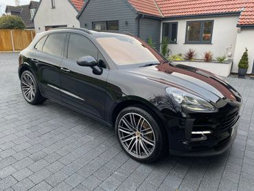 Black Porsche SUV parked on a modern driveway in front of a house.