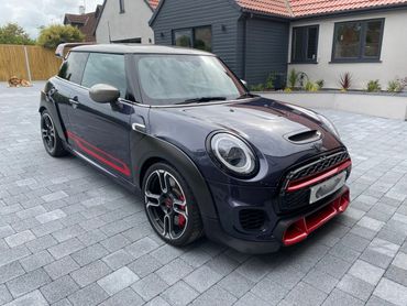 Sleek Mini Cooper with black and red accents parked on a stone driveway.