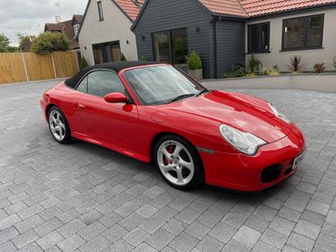 Red Porsche convertible parked on gray brick driveway near modern houses.