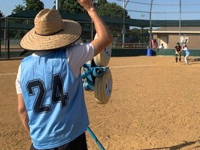 The pitching machine sending baseballs to the plate where a batter and catcher await to play.