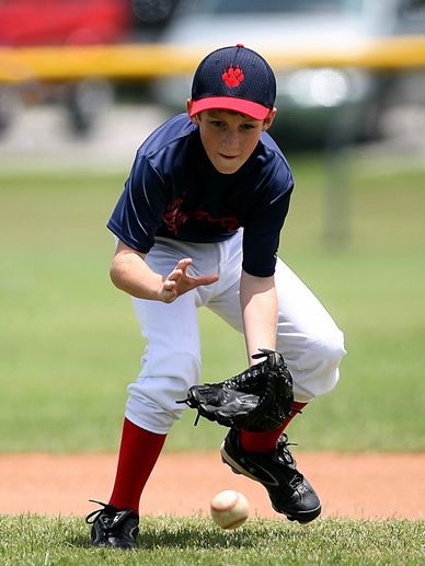 A boy about to field a baseball on the ground with his glove at shortstop