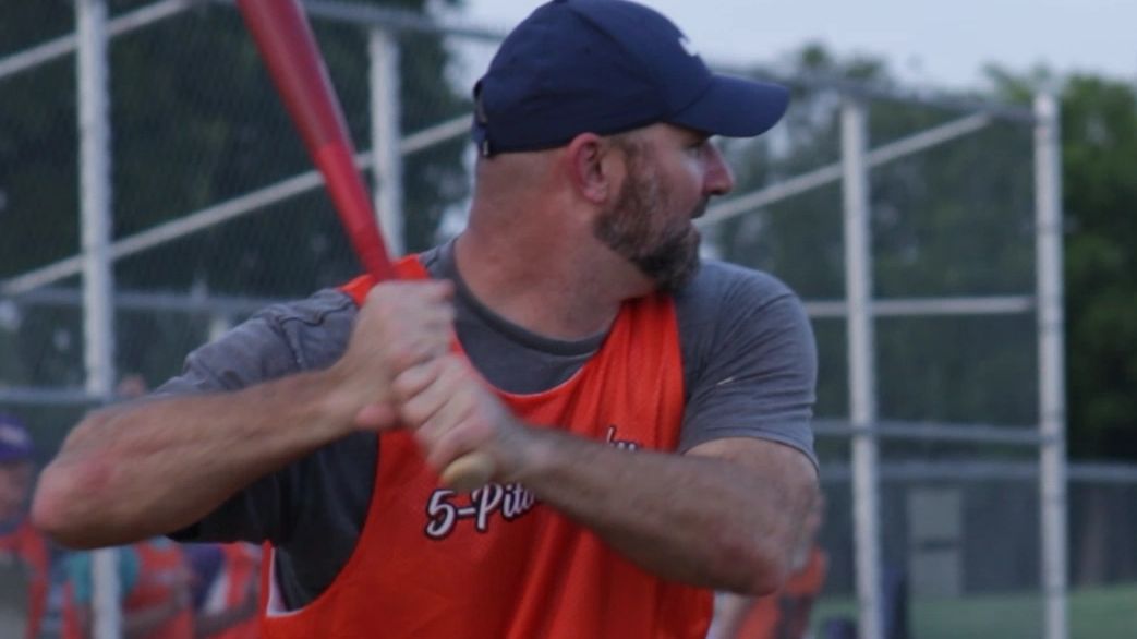 An adult male playing 5-Pitch Plucky® with a red bat at the plate getting ready to swing and hit.
