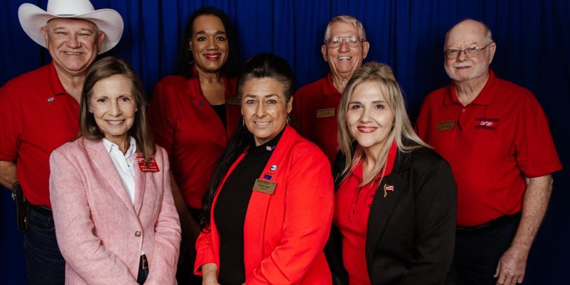 Group of seven people posing, most in red shirts.
