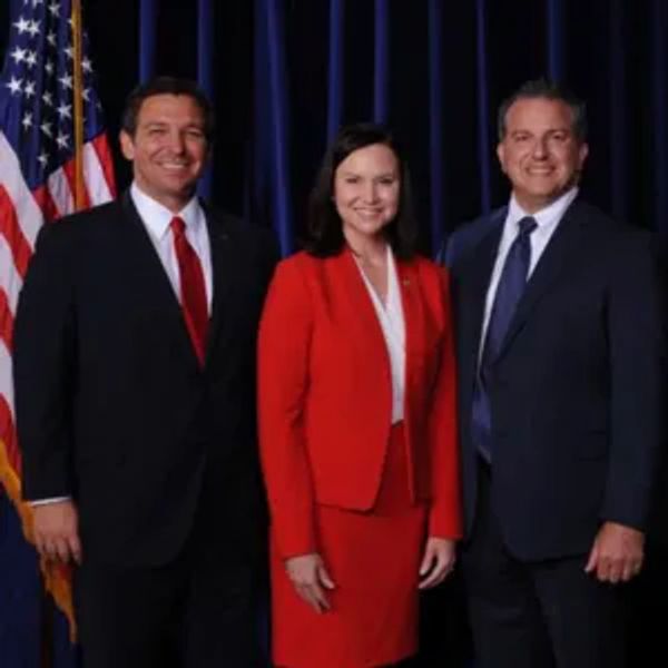 Three people in formal attire with an American flag.