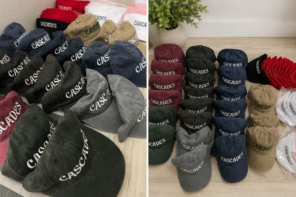 Multiple colored caps with 'CASCADES' logo arranged on a wooden floor.