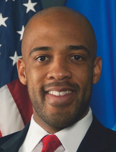 Portrait of a smiling man in a suit with an American flag background.