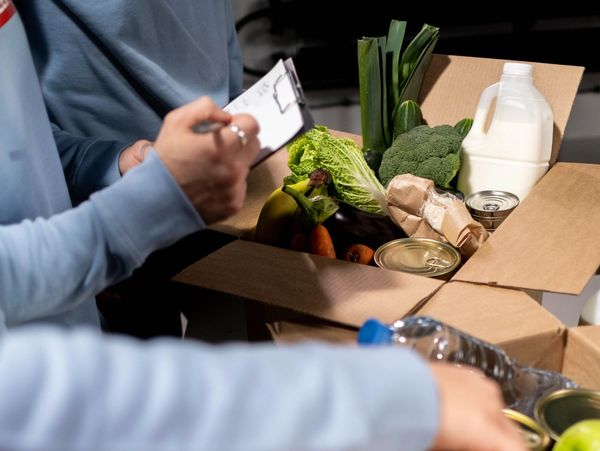 People packing fresh groceries into cardboard boxes.