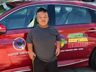 A boy standing in front of a car