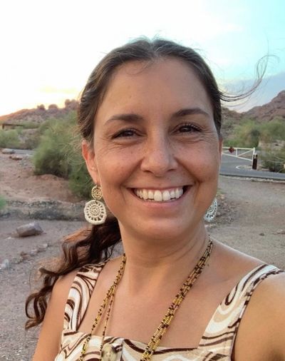 Smiling woman outdoors with desert landscape in background.