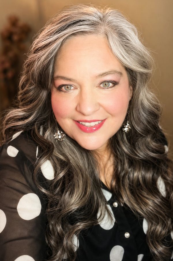 Smiling woman with long, wavy gray hair and polka dot blouse.