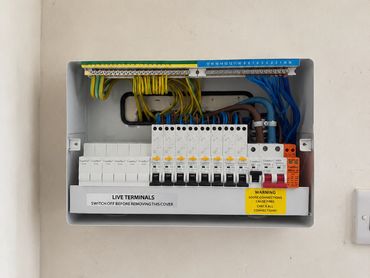 Electrical fuse box with labeled switches and warning signs on a beige wall.