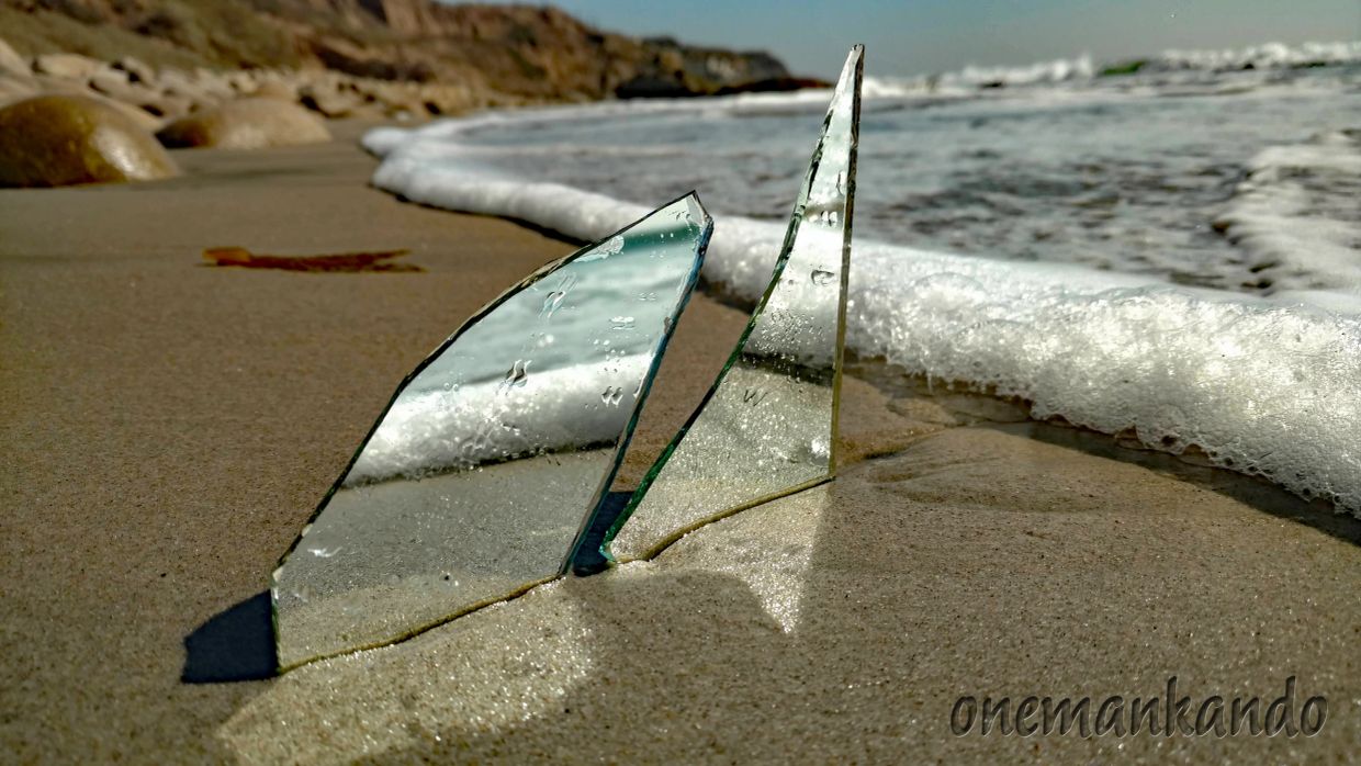 Two glass shards on a sandy beach near the ocean waves.