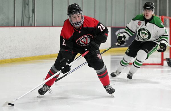 Hockey player in black and red uniform controlling the puck on ice.