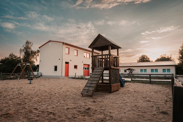 Empty playground with wooden climbing structure and houses at sunset.