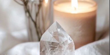 Clear quartz crystal with a lit candle in the background on a soft surface.