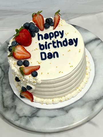 White birthday cake with fresh strawberries and blueberries, saying 'happy birthday Dan'.