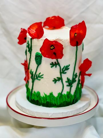 Tall white cake decorated with red poppy flowers and green stems.