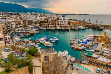 A scenic harbor filled with boats and surrounded by a coastal town with mountains in the background.