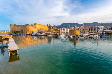Historic harbor with boats and a large stone fortress under a blue sky.