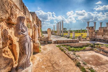 Ancient ruins with statues and tall columns under a bright blue sky.