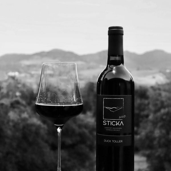 A bottle of Sticka Cabernet Sauvignon wine with a filled glass outdoors.