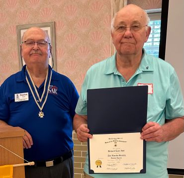 Two elderly men, one holding a certificate.