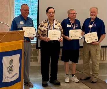 Four men proudly holding framed certificates at an award event.