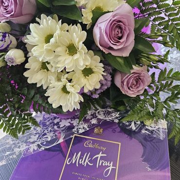 A bouquet of flowers with a Cadbury Milk Tray chocolate box.