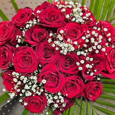 A vibrant bouquet of red roses accented with white baby's breath and green leaves.